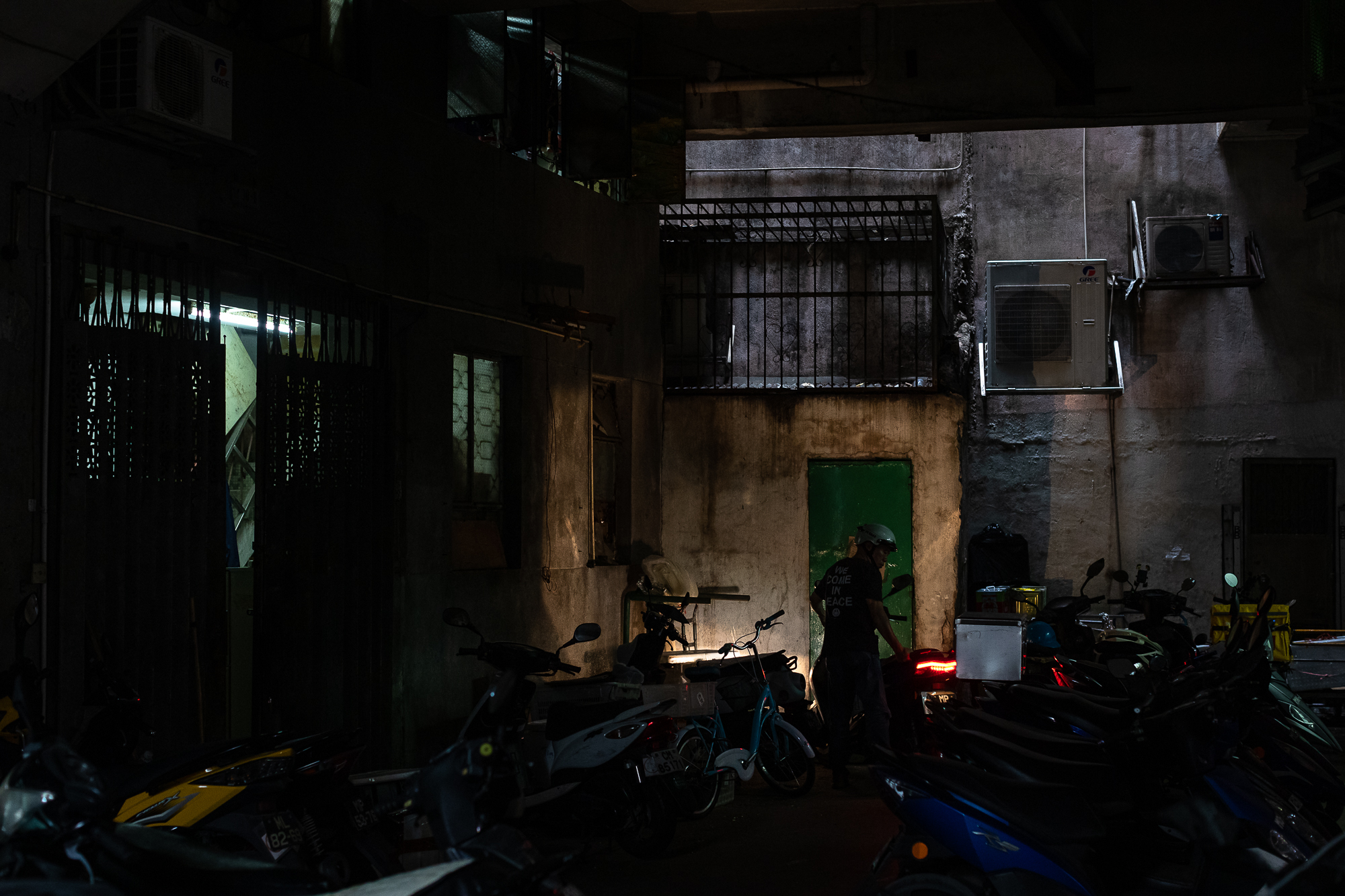 A rider readies his motorbike in an alley as daylight struggles to penetrate through the densely packed buildings