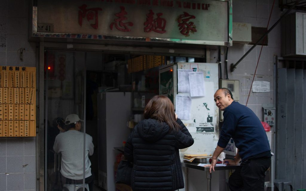 Chio Chi Ngong, right, greets a customer outside the A Chi ramen shop near the Ruins of St. Paul’s