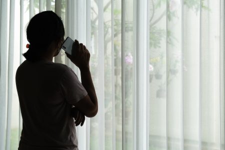 Woman standing by a window holding a phone