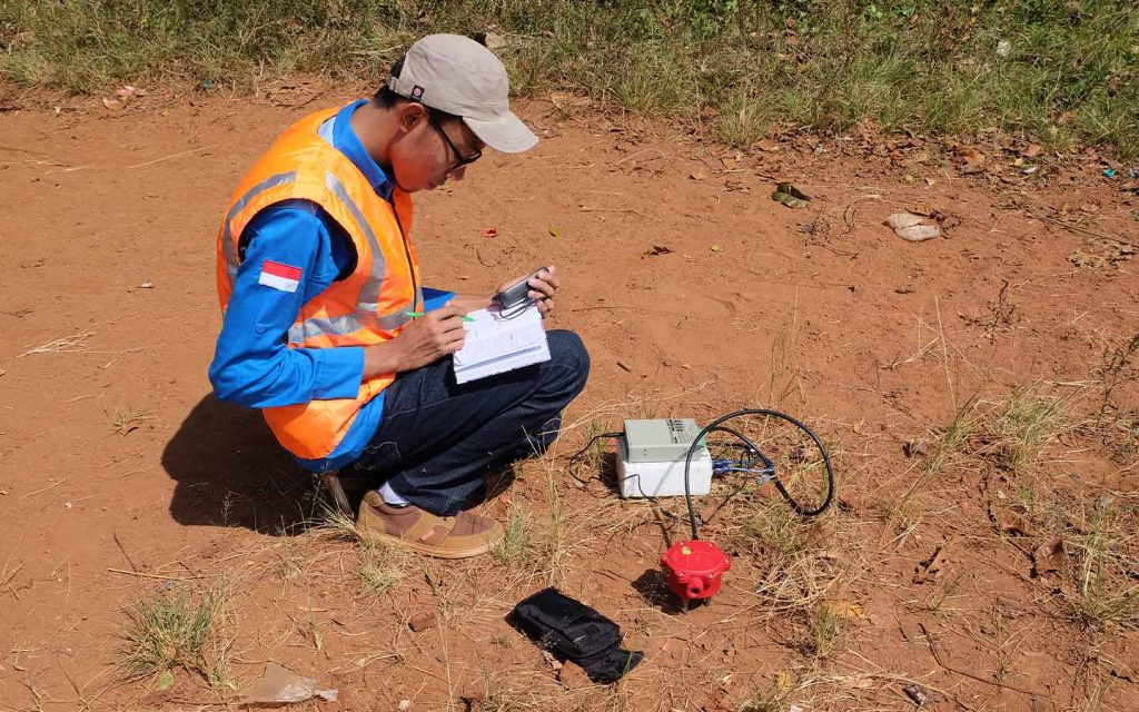 A scientist uses a data logger and geophone to measure field vibrations, looking to identify seismic vulnerabilities