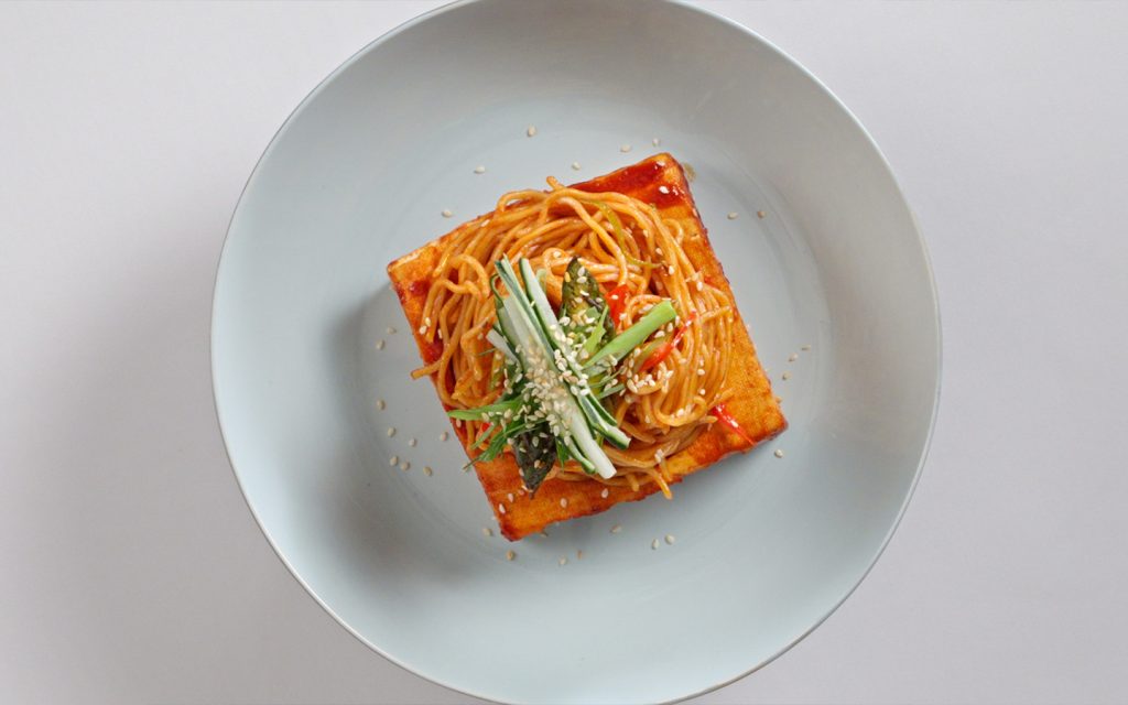 Ramen noodles burst from a hollowed-out gochujang-glazed tofu “tower” - a wild Culinary Class Wars-inspired creation
