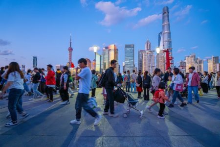 Consumers walk along Shanghai’s famous Bund, with the Pudong business district looming behind them